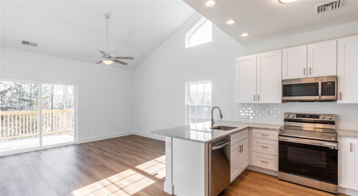 Kitchen featuring light wood-type flooring, kitchen peninsula, light stone counters, appliances with stainless steel finishes, and sink
