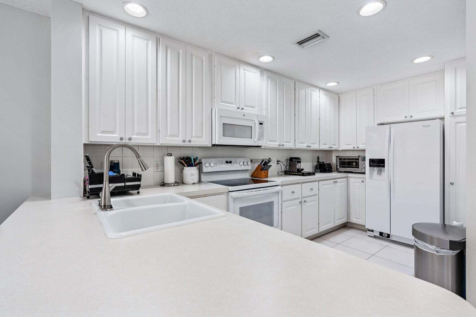 4030 Parkside Drive Jupiter, FL 33458 - Photo 6 of 26 a kitchen with granite countertop a refrigerator sink and white cabinets