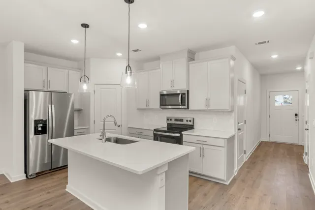 a kitchen with stainless steel appliances a stove a sink a refrigerator and white cabinets with wooden floor