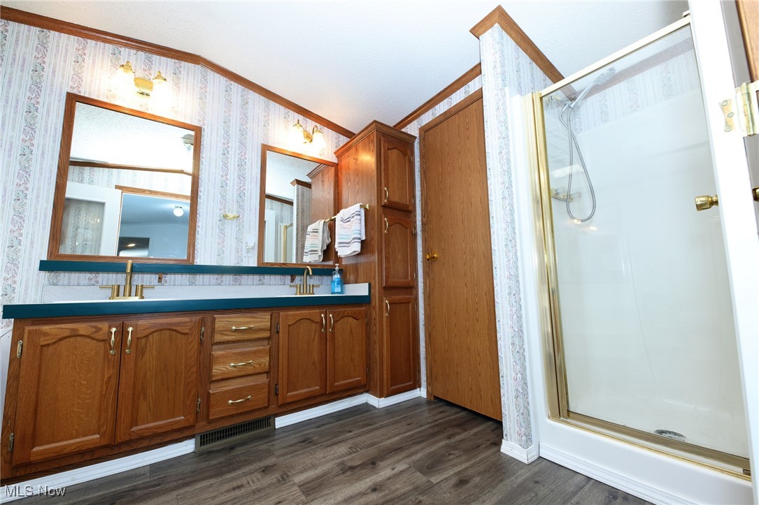 211 Gibson Road New Cumberland, WV 26047 - Photo 17 of 46 Bathroom featuring a stall shower, double vanity, crown molding, dark wood-type flooring, and wallpapered walls