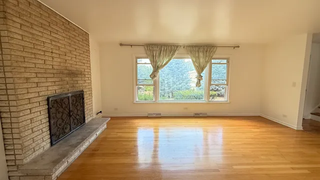 an empty room with wooden floor fireplace and windows