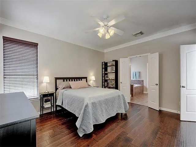 1832 Nelson Ranch Loop Cedar Park, TX 78613 - Photo 14 of 15 Rich hardwood flooring grounds this inviting bedroom, connecting seamlessly to a well-appointed primary bathroom beyond double doors.