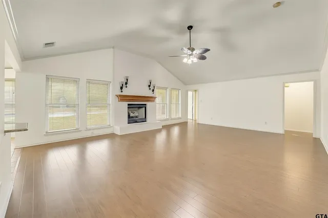 an empty room with wooden floor fireplace and windows
