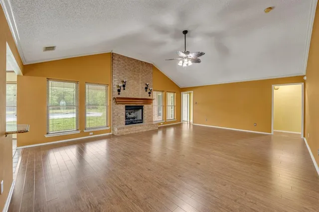 an empty room with wooden floor fireplace and windows