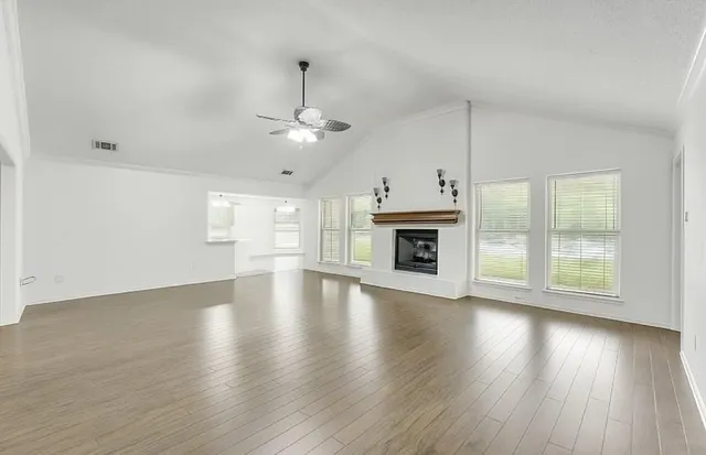an empty room with wooden floor fireplace and windows