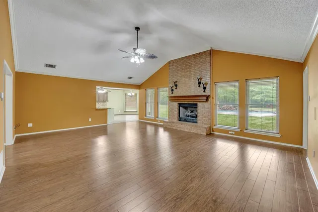 an empty room with wooden floor fireplace and windows