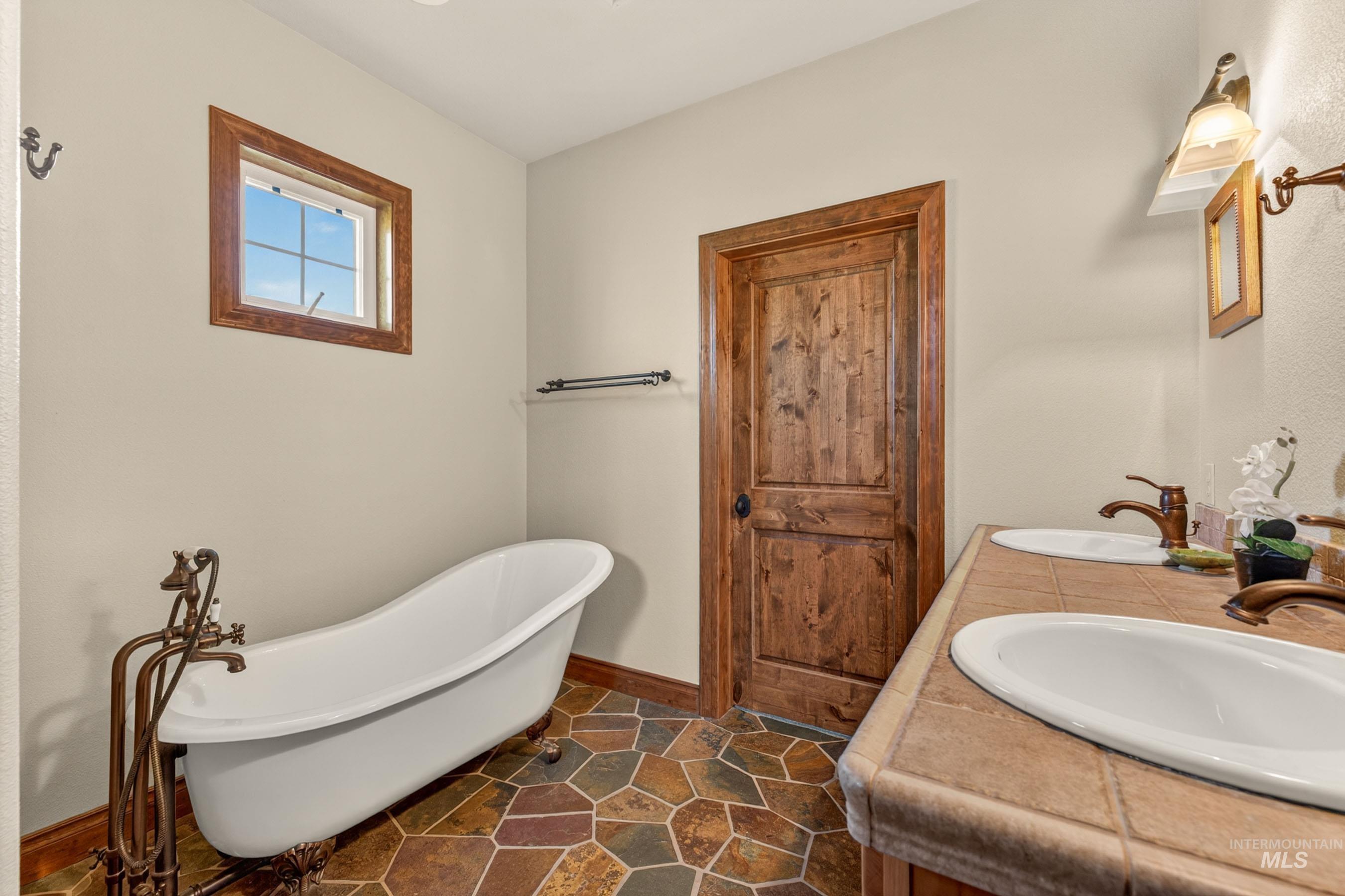 113 Deford Road White Bird, ID 83554 - Photo 20 of 49 Clawfoot tub with floor-mounted faucet, dual vessel sinks, tile countertop, and wood-finish door