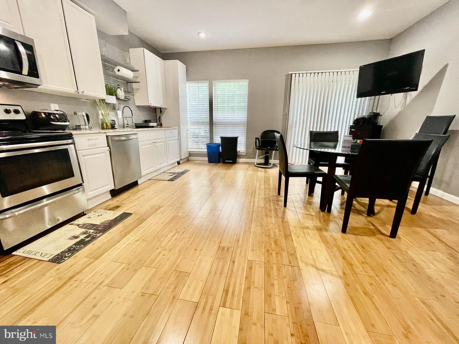 a open kitchen with stainless steel appliances kitchen island granite countertop a stove top oven a sink dishwasher and white cabinets with wooden floor
