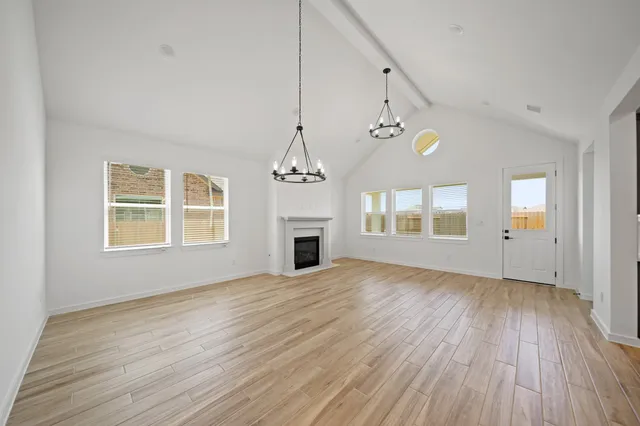 an empty room with wooden floor chandelier and windows
