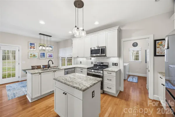 a kitchen with stainless steel appliances granite countertop a stove top oven a sink dishwasher and a refrigerator with wooden floor