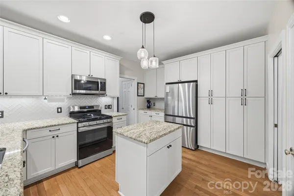 a kitchen with stainless steel appliances granite countertop a refrigerator oven a sink dishwasher and white cabinets with wooden floor