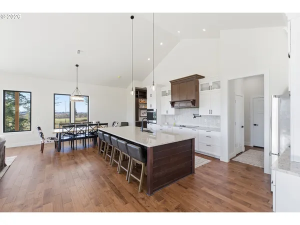 a living room with stainless steel appliances kitchen island granite countertop a sink a stove a dining table and chairs with wooden floor