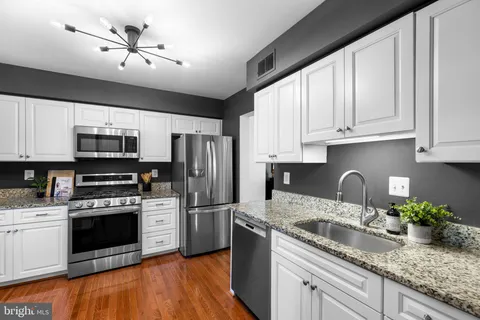 a kitchen with granite countertop a sink stainless steel appliances and white cabinets