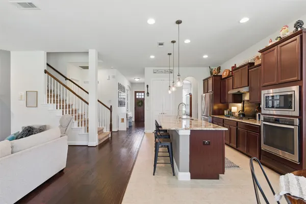 a kitchen with stainless steel appliances kitchen island granite countertop a refrigerator a stove and a sink with wooden floor