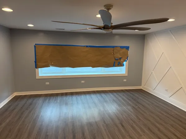 an empty room with wooden floor fan and windows