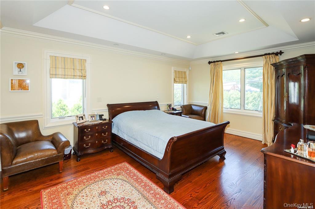 24 Steamboat Road Great Neck, NY 11024 - Photo 17 of 28 Bedroom with a tray ceiling, multiple windows, ornamental molding, wood finished floors, and recessed lighting