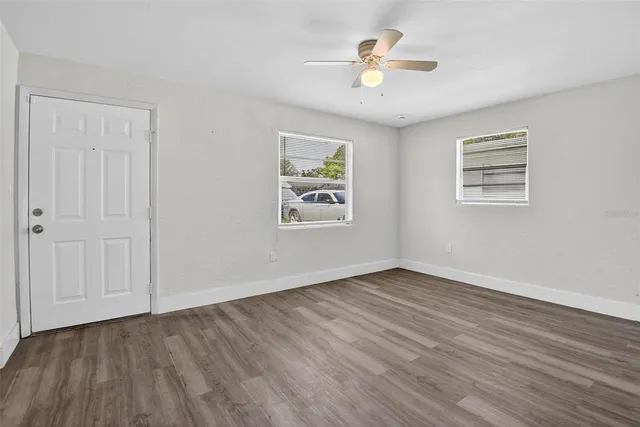 a view of an empty room with wooden floor and a ceiling fan