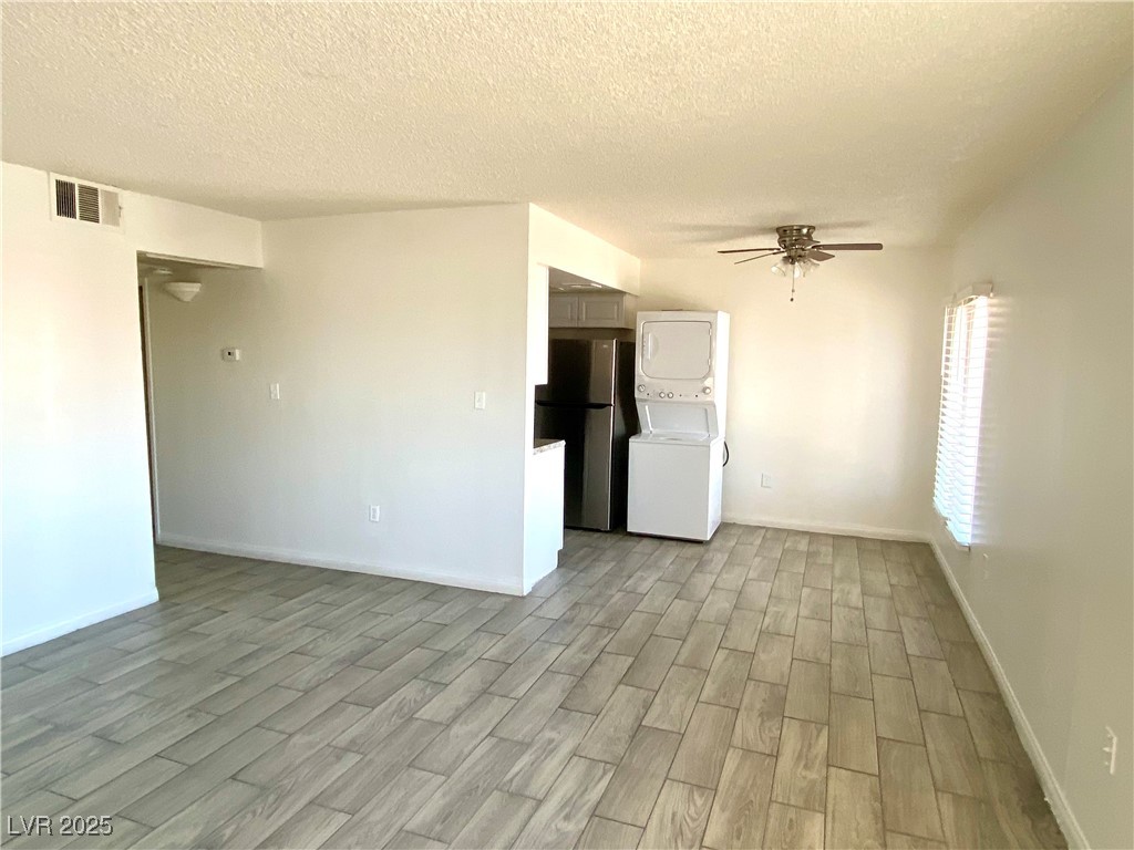 6213 Smoke Ranch Road Las Vegas, NV 89108 - Photo 8 of 22 Unfurnished living room featuring stacked washer and clothes dryer, light wood-style flooring, ceiling fan, and a textured ceiling