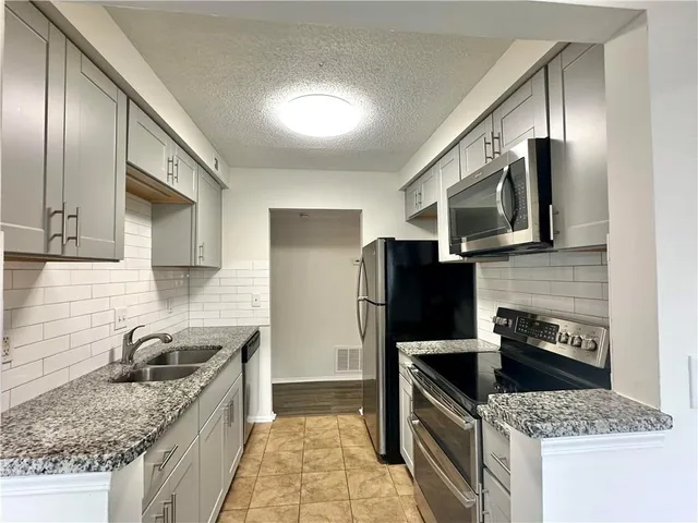 a kitchen with granite countertop stainless steel appliances a sink stove refrigerator and cabinets