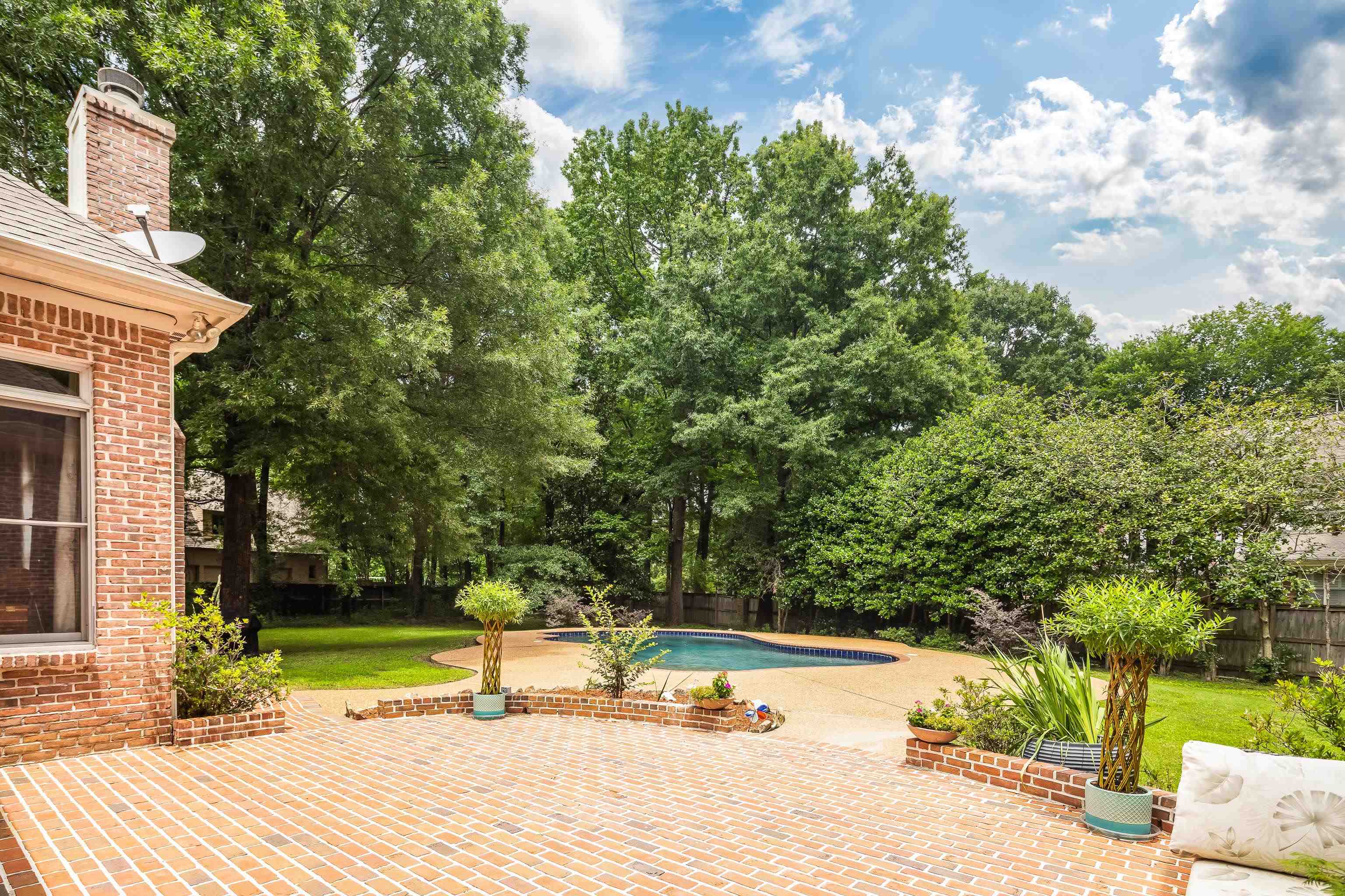 350 Bluff Ridge Cove Memphis, TN 38018 - Photo 34 of 37 Expansive brick patio featuring a curved retaining wall, a kidney-shaped swimming pool, mature perimeter trees, and a well-maintained lawn