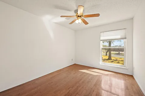 an empty room with wooden floor fan and windows