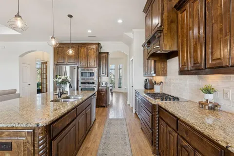 a kitchen with granite countertop kitchen island stainless steel appliances a sink a counter top space a stove and a wooden floors