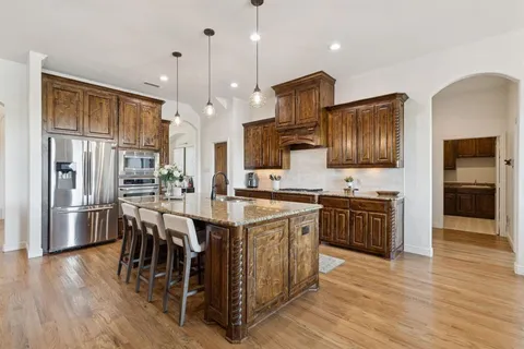 a kitchen with stainless steel appliances kitchen island granite countertop a refrigerator a stove top oven a sink dishwasher and white cabinets with wooden floor