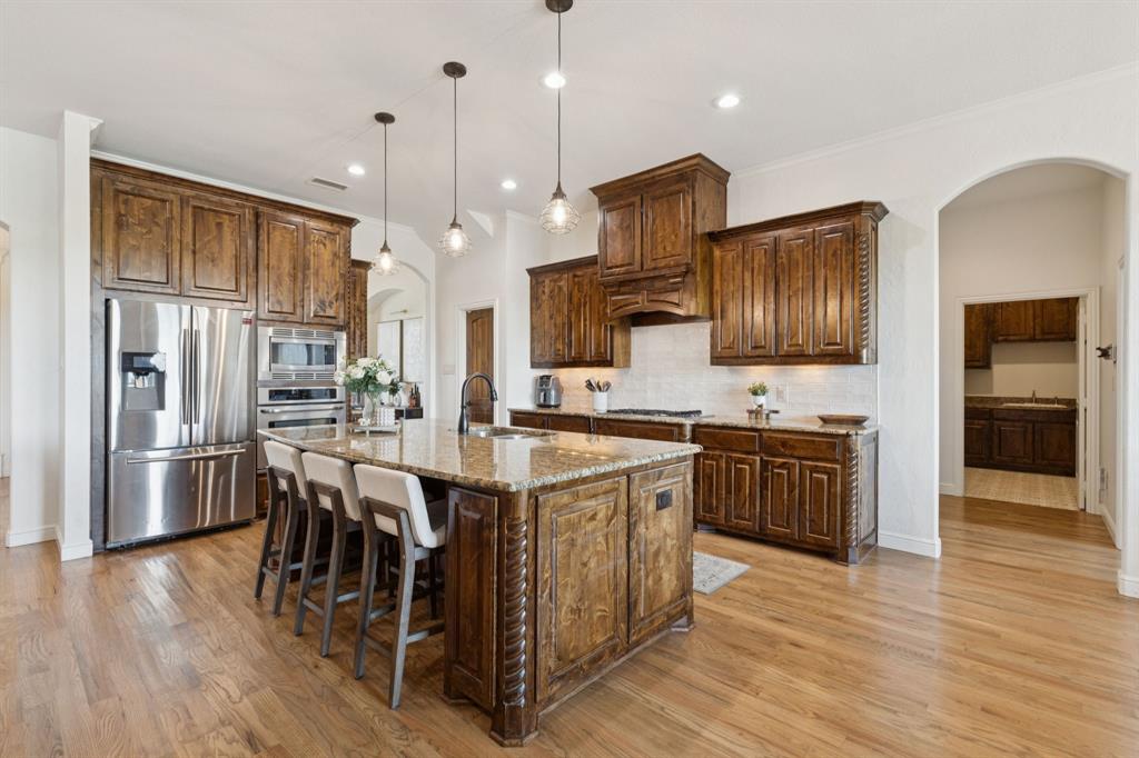 6824 Katie Corral Drive Fort Worth, TX 76126 - Photo 9 of 39 a kitchen with stainless steel appliances kitchen island granite countertop a refrigerator a stove top oven a sink dishwasher and white cabinets with wooden floor