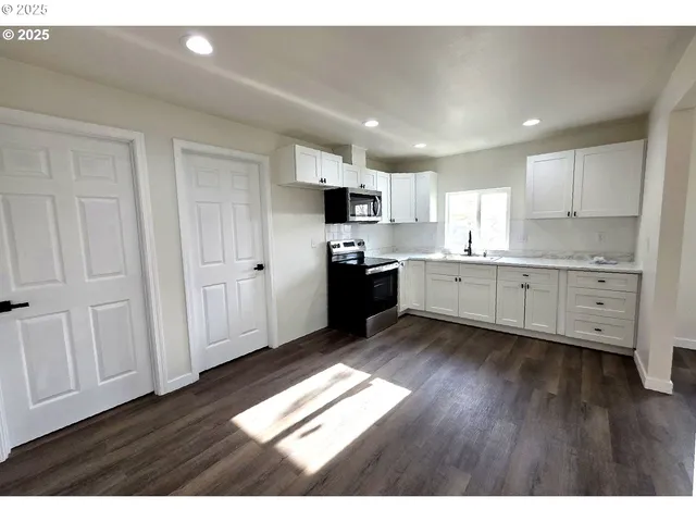 a kitchen with stainless steel appliances granite countertop a refrigerator a sink dishwasher and white cabinets with wooden floor