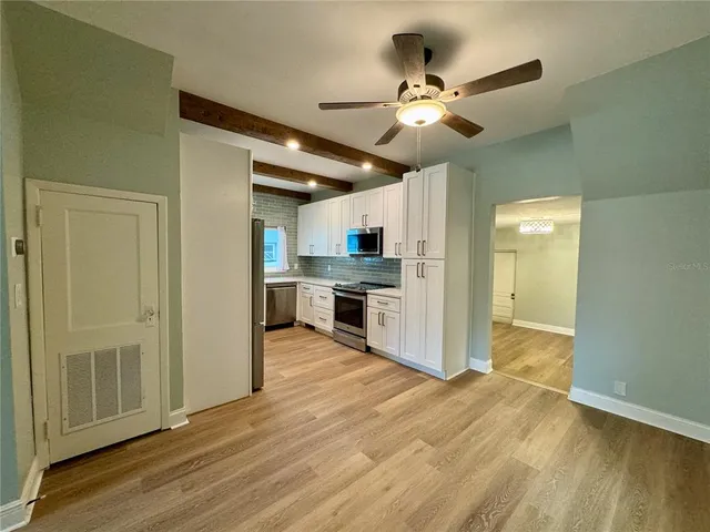 a view of a livingroom with a ceiling fan & kitchen space