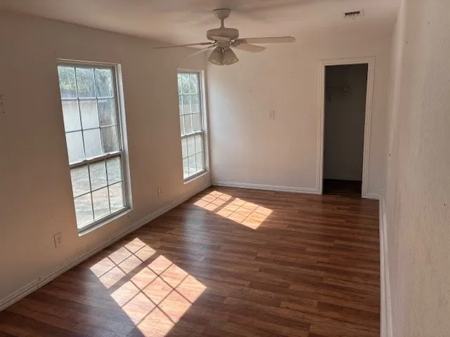 an empty room with wooden floor chandelier fan and windows