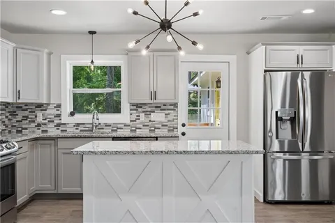 a kitchen with stainless steel appliances granite countertop a refrigerator a sink dishwasher a stove and white cabinets with wooden floor