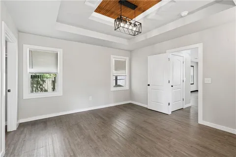 an empty room with wooden floor chandelier fan and windows