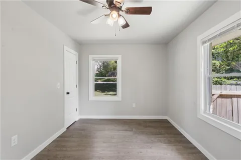 an empty room with wooden floor chandelier fan and windows
