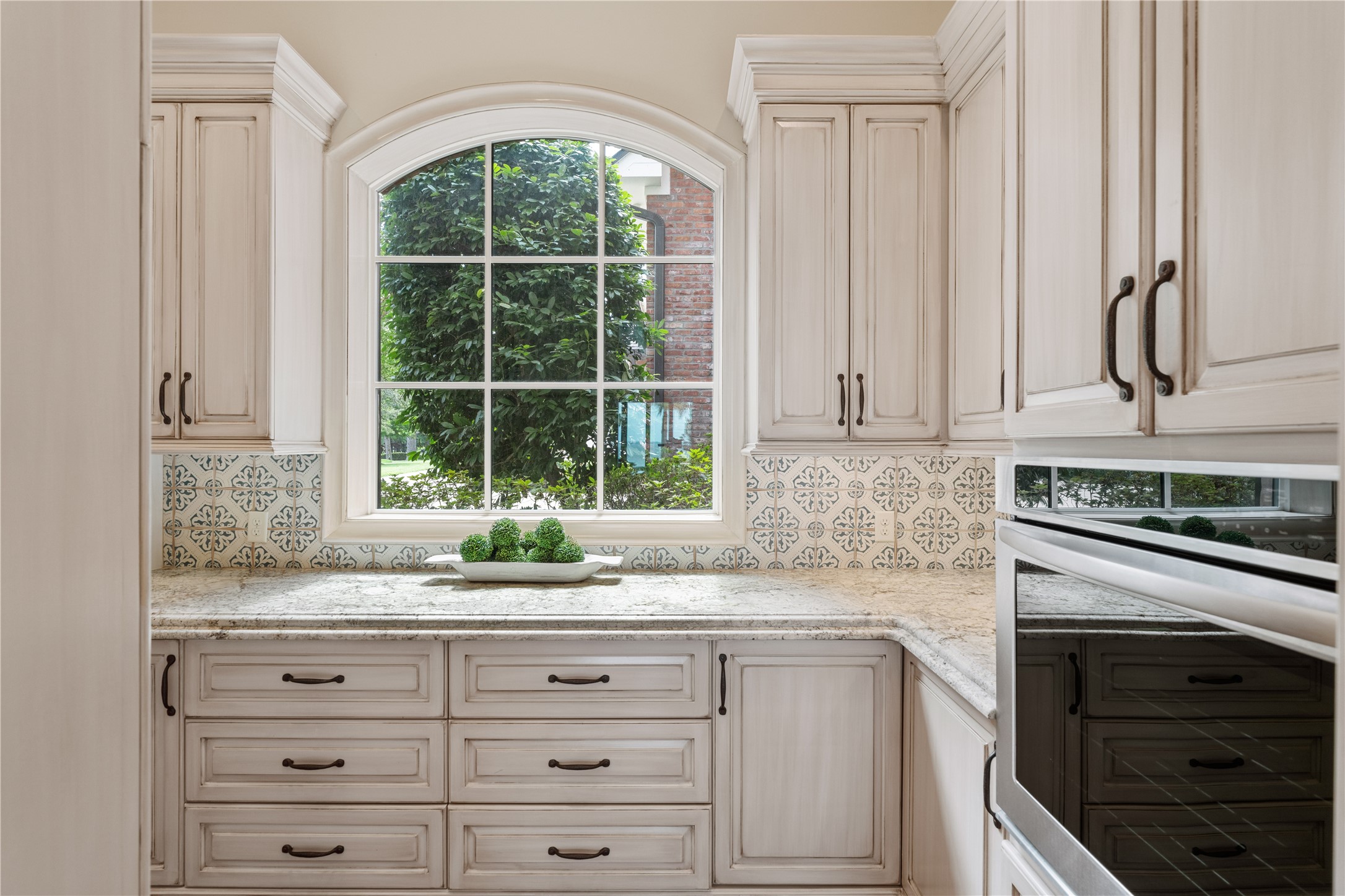 12349 Longmire Trace Conroe, TX 77304 - Photo 9 of 48 Sunlit butler's pantry features an arched window, granite countertops, and detailed patterned tile backsplash.
