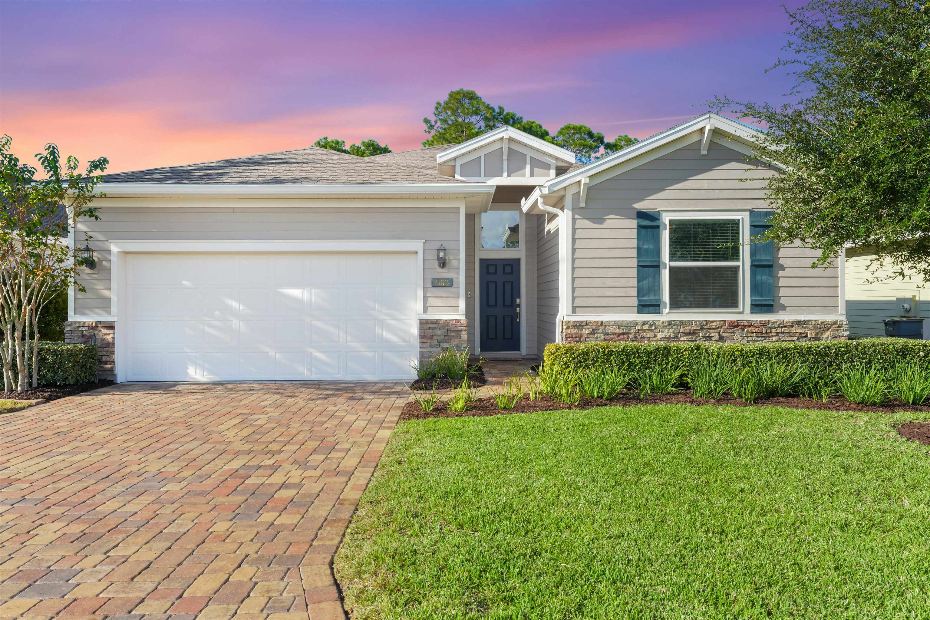 View of front of home featuring stone siding, a yard, decorative driveway, and an attached garage