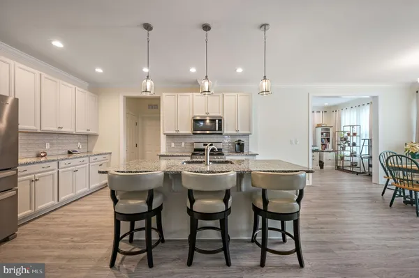 a kitchen with kitchen island granite countertop a refrigerator a stove a sink and white cabinets with wooden floor