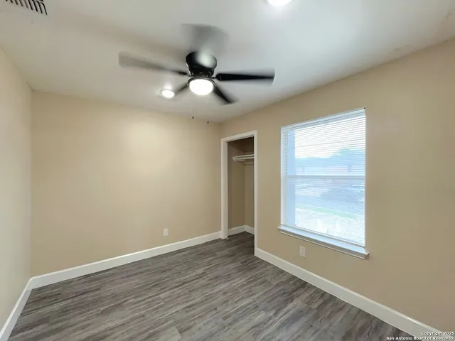 an empty room with wooden floor fan and windows
