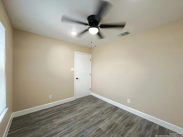 an empty room with wooden floor ceiling fan and window
