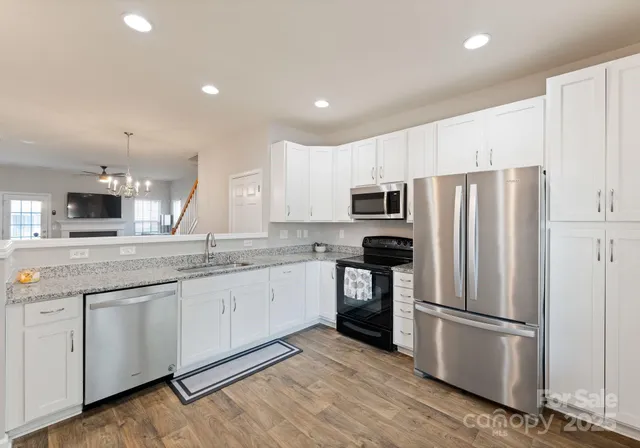 a kitchen with granite countertop stainless steel appliances a refrigerator a sink and white cabinets