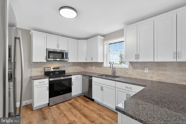 a kitchen with granite countertop a sink stainless steel appliances and white cabinets