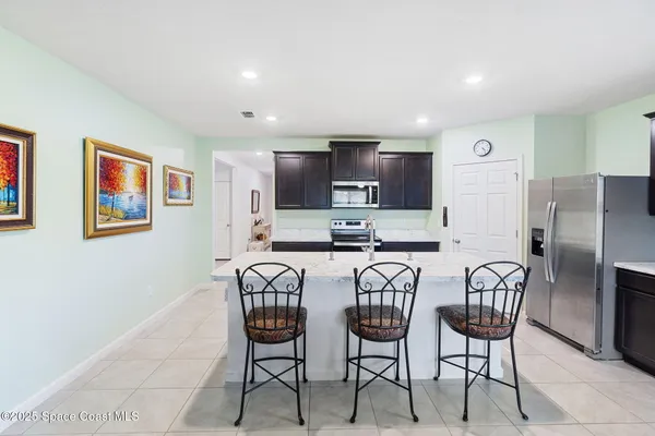 a kitchen with stainless steel appliances granite countertop a dining table chairs refrigerator and microwave