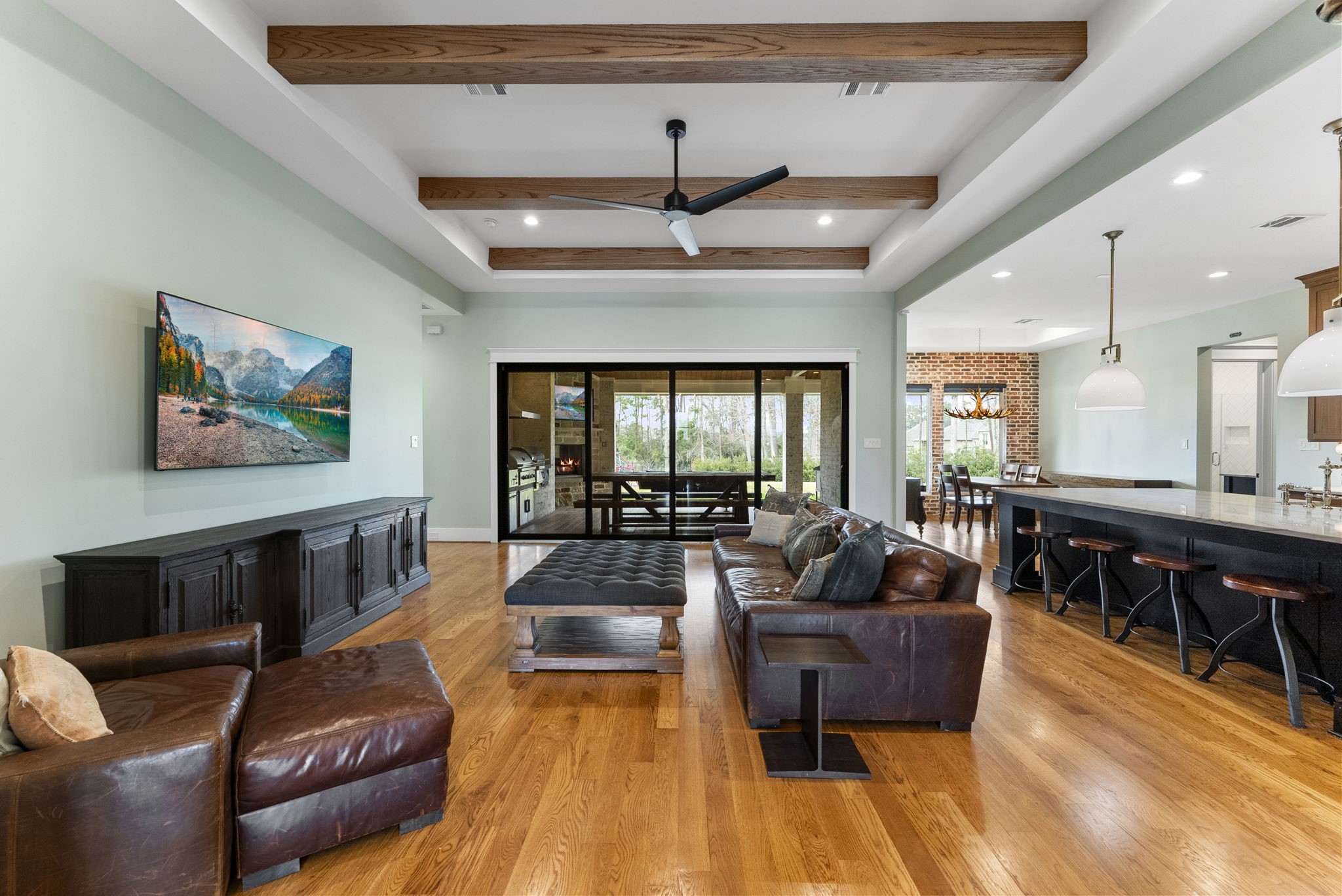 14019 Beartooth Bend Trail Conroe, TX 77384 - Photo 8 of 28 Spacious open-concept living room featuring hardwood floors, wood beam ceiling details, and large sliding glass doors that open seamlessly to the covered patio
