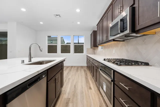 a kitchen with stainless steel appliances granite countertop a sink a stove and a wooden floors