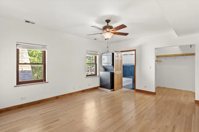an empty room with wooden floor chandelier fan and windows
