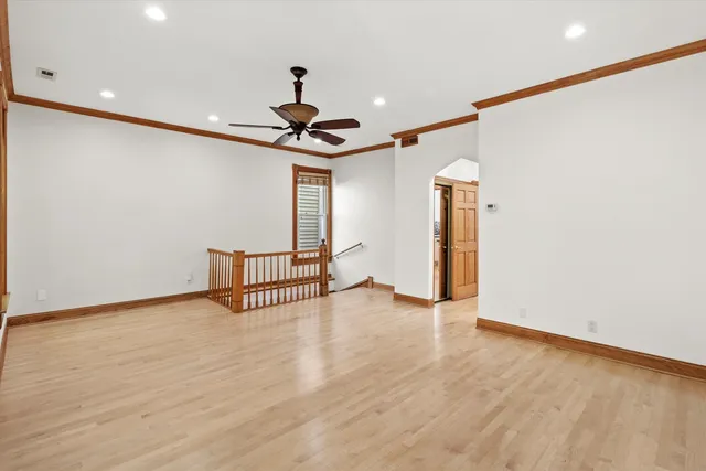 a view of an empty room with wooden floor and a ceiling fan