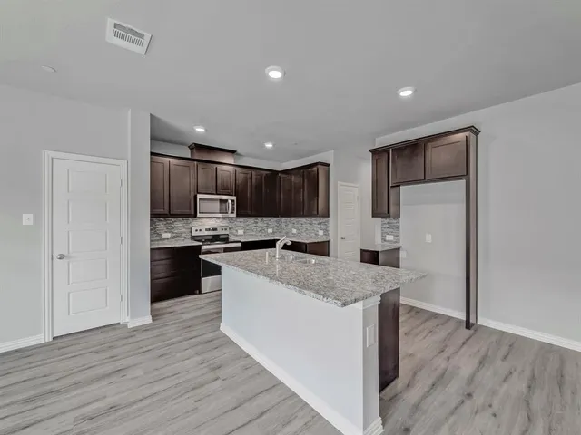 a kitchen with stainless steel appliances granite countertop white cabinets a refrigerator a sink a stove a microwave and island with wooden floor