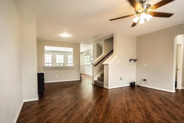 an empty room with wooden floor chandelier fan and windows