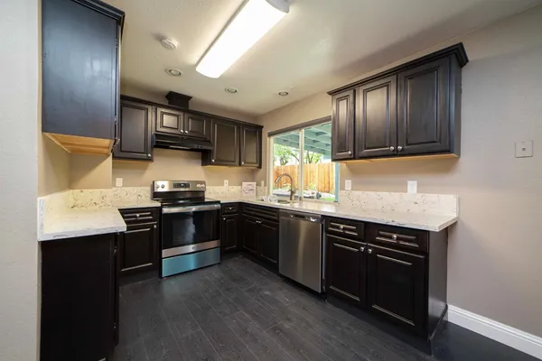 a view of a kitchen with stainless steel appliances granite countertop a refrigerator a stove top oven a sink dishwasher and wooden floor