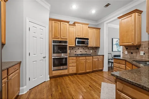 a large kitchen with stainless steel appliances granite countertop a stove a sink dishwasher a microwave oven and a refrigerator with wooden floor